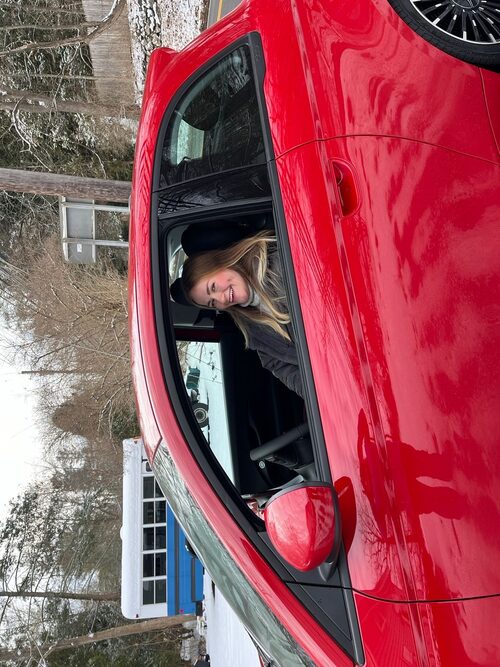 Anna smiling behind the wheel of her car in the snow