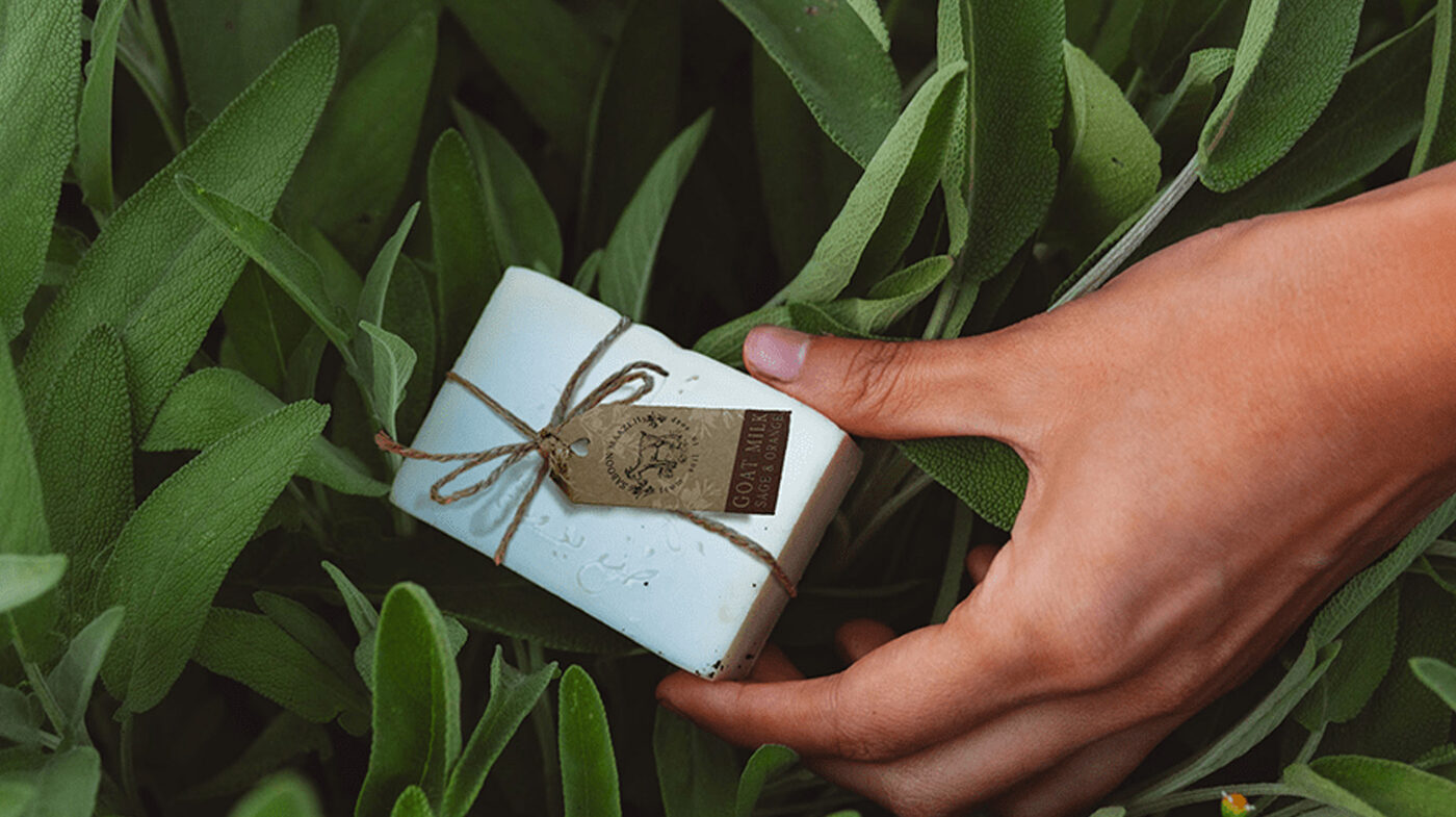 Saboon Maazeh packaging: a soap bar wrapped in brown paper and twine, tucked into a bed of herbs